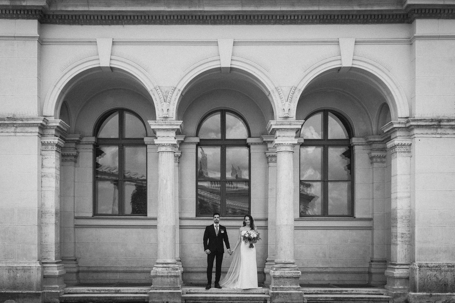 Esküvői pár egy elegáns épület árkádjai előtt